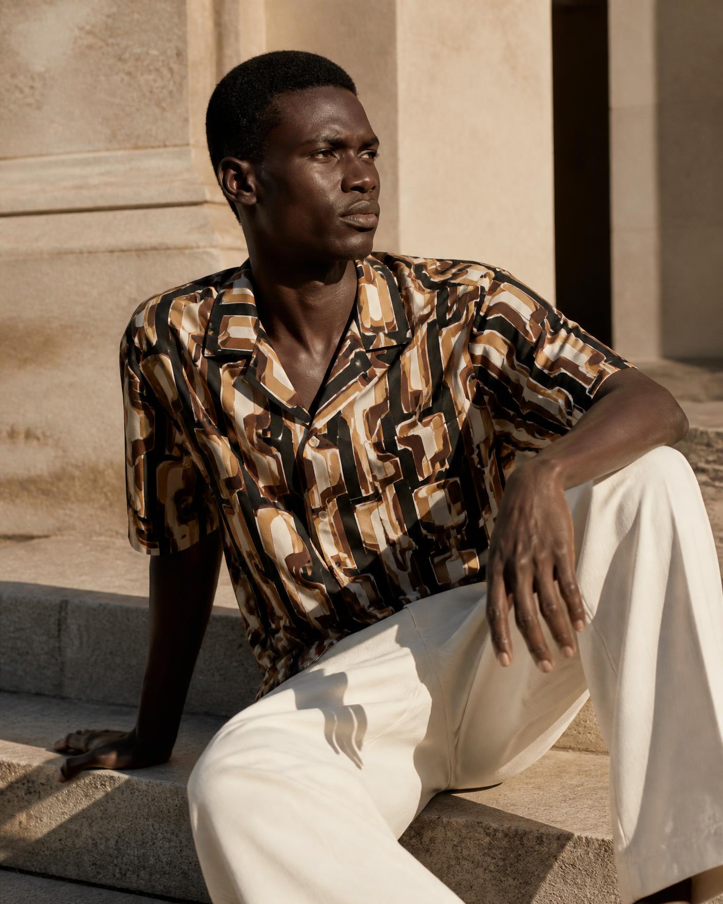 African model wearing the Retro Geometric Print Cuban Collar Shirt seated on stone steps